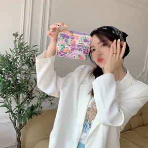 Fashionable floral makeup bag with purple zipper and woven label held by a stylish woman