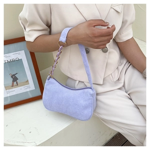 Detail of purple corduroy shoulder bag showing gold chain link and ribbed texture