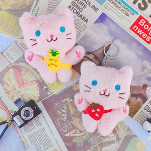 Close-up of pink plush cat keychains with small pineapple and strawberry bag accessories
