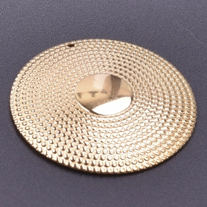 Macro shot of 18k gold plated round charm with dotted texture and central smooth finish