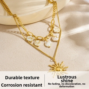 Detail of gold layered necklace featuring sun pendant and white marble discs on sand