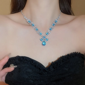 Close-up of a silver necklace featuring a large pear-cut blue zircon pendant on a model
