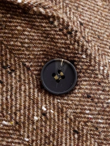 Vue macro du tissu en tweed à chevrons marron avec un bouton noir à quatre trous