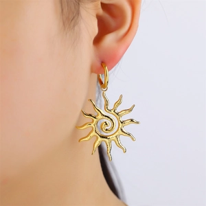 Detail view of golden sun-shaped earrings with spiral center worn by a model