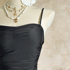 Detail of black pleated bikini top with slim straps and elegant draped fabric texture