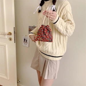 Floral drawstring pouch with vintage patterns held by a woman in a beige knit sweater
