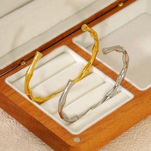 Bamboo-style open bangle in gold and silver finish on a wooden jewelry display case