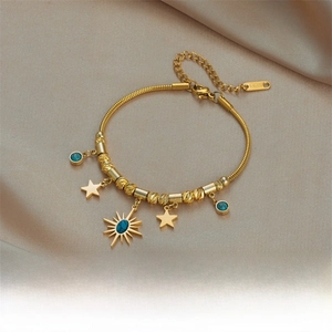 Detail of gold titanium steel bracelet with turquoise sun and star charms on silk