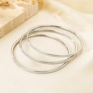 Minimalist polished stainless steel bangles set on aesthetic neutral fabric background