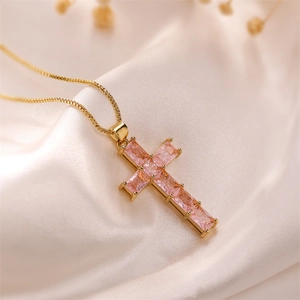 Macro shot of gold cross necklace with pink zircon gemstones on beige silk fabric