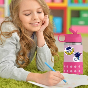 Pink kids water bottle with cute astronaut stickers and straw in a cozy room