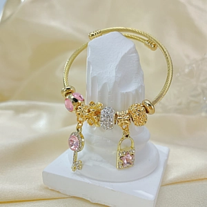 Close-up of golden twisted cuff bracelet with pink gemstone lock and key charms