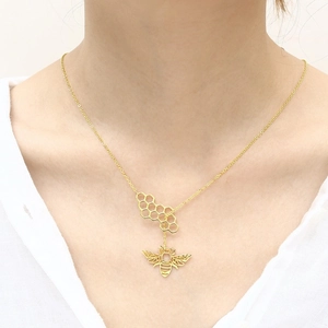 Detail of gold necklace with hexagonal honeycomb and bee pendant worn on a model