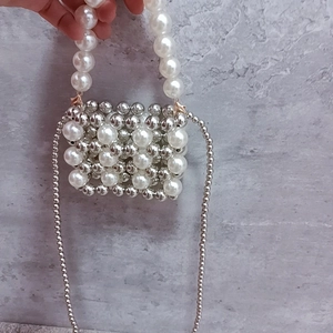 Detail of a mini beaded handbag with white pearls and silver beads held by hand
