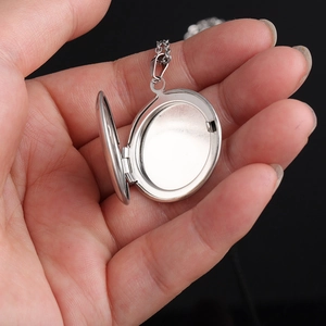 Close-up of open 316L stainless steel locket necklace held in hand on black background