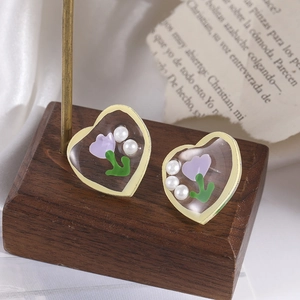 Macro shot of gold heart earrings with purple tulips and pearls on a wooden stand