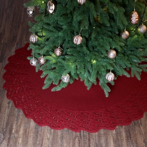 Knitted dark red Christmas tree skirt with wavy edges on dark wood floor scenery