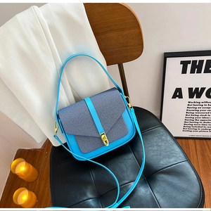 Close-up of sky blue shoulder bag with woven fabric flap and gold metal twist lock
