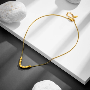 Titanium steel necklace with seven oval gold beans on a minimalist black and white surface