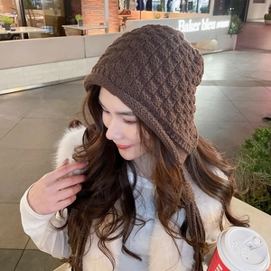 Detail of dark brown chunky knit earflap hat with checkered texture and tassels
