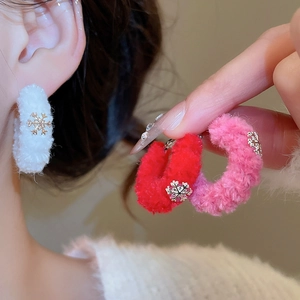 Close-up of winter velvet hoop earring with golden snowflake detail on white plush fabric