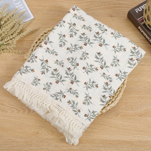 Close-up of double-layer cotton baby blanket with green leaf patterns and cream tassels
