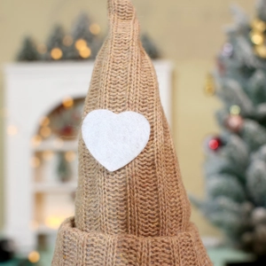 Detail of a brown knitted Christmas gnome hat featuring a white felt heart ornament