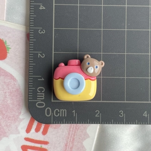 Close-up showing a 2cm small resin camera charm with a bear head for DIY craft projects