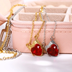 Macro detail of red heart zircon necklaces with metal wing design in gold and silver