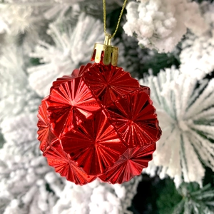 Macro shot of faceted bright red Christmas ball ornament hanging on a snowy tree branch