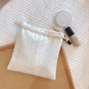 Macro detail of white lace embroidery drawstring storage bag on a wooden tray