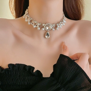 Detail of floral necklace with rhinestones and a teardrop pearl pendant on a model