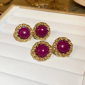 Close-up of vintage gold woven earrings with central purple gemstone on a white stand