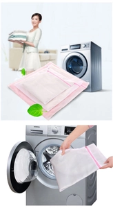 Detailed view of hand placing a white mesh laundry bag with pink zipper into a washing machine