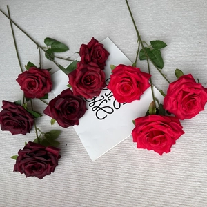 Close-up of deep burgundy and bright red artificial silk roses with green leaves on a table