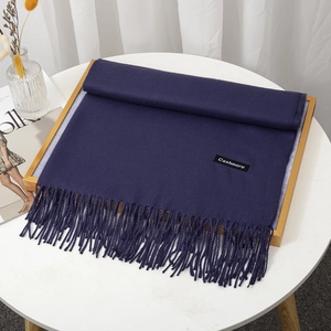 Detailed view of dark blue cashmere scarf with tassels and label on a white table