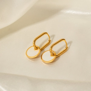 Macro view of 18K gold earrings with white shell pendants on a white satin background