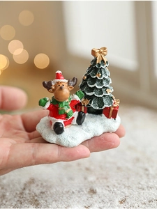 Close-up of a mini resin Christmas deer and tree figurine held by hand for scale