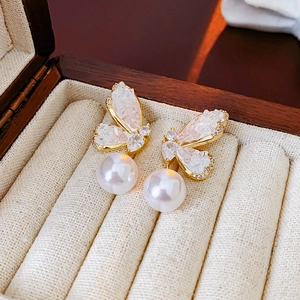 Detail of gold butterfly earrings with sparkling crystals and a large white pearl drop