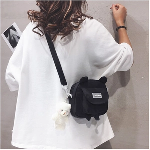 Close-up of a black canvas crossbody bag with a cute bear pendant on a female model