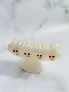 Detailed view of pearlescent acetate hair claw clip with sparkling rhinestone cherry patterns