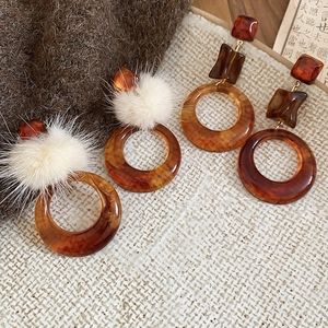 Dettaglio di orecchini in resina ambrata con pompon di pelliccia e texture retro