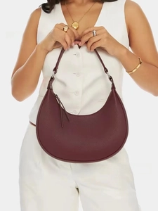 Detail of burgundy crescent shoulder bag with pebbled leather texture and silver hardware