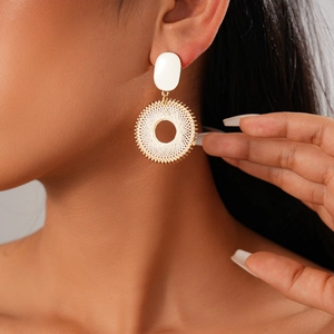 Detail of a gold circular mesh earring with white geometric oval stud on a model