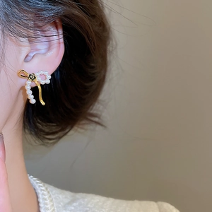 Detail of bow-shaped earring with pearl, 18k gold plating, and black flower motif
