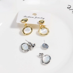 Détail des boucles d'oreilles ovales en nacre or et argent sur une assiette en céramique