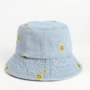 Detail of yellow smiley face embroidery on light blue washed denim bucket hat