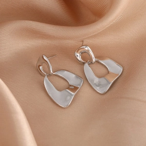 Macro detail of geometric silver hoop earrings resting on elegant beige silk fabric