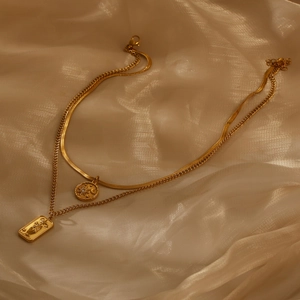 Detail of gold double-layered necklace with sun coin and tarot flower pendant on beige silk