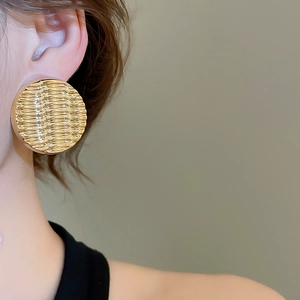 Macro view of gold round ripple textured acrylic stud earrings worn by a model